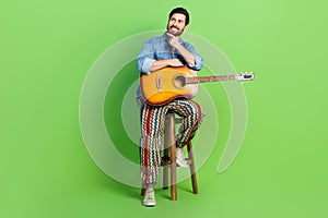 Full length photo of thoughtful good mood guy dressed jeans shirt playing guitar looking empty space  green