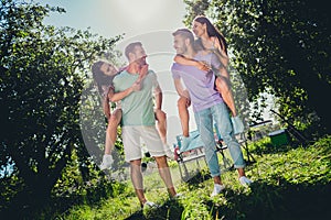 Full length photo of two couples buddies sitting piggyback looking each other outdoors outside backyard forest