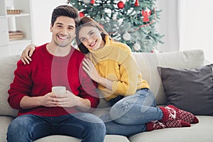 Full length photo of two romantic people sit on divan couch man hold mug woman hug wear red knitted soft socks enjoy