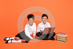 Full length photo of two young afro school kids learn online laptop student isolated over orange color background