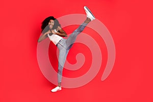Full length photo of young attractive black girl fight battle kick leg sporty isolated over red color background