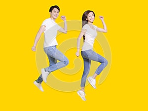 Full length photo of young couple jumping and running isolated yellow color background