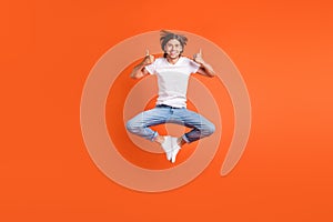Full length photo of young funky happy man jump up good mood thumbs up isolated on orange color background