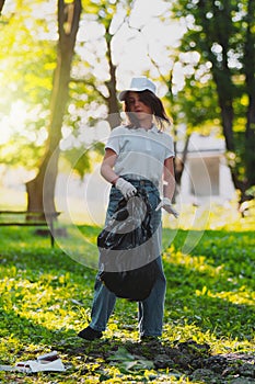 Full-length photo of a young girl volunteer standing in casual clothes holding black garbage bag in her hands and