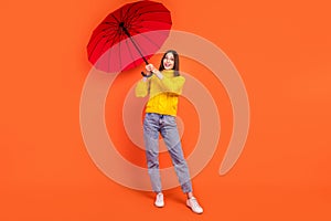 Full length photo of young woman happy positive smile windy umbrella wet autumn isolated over orange color background
