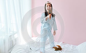 Full-length of a playful little girl in pajama holding a hair brush like microphone singing imitates herself a real singer in the