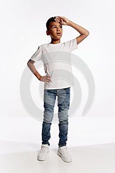 Full-length portrait of african little boy in white tee looking up isolated over white background. Kids emotions concept