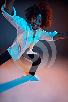 Full-length portrait of African young girl casual clothes, outfit isolated on dark blue studio background in pink neon