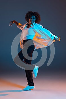 Full-length portrait of African young girl casual clothes, outfit isolated on dark blue studio background in pink neon