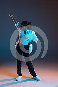 Full-length portrait of African young girl casual clothes, outfit isolated on dark blue studio background in pink neon