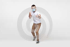 Full length portrait of aggressive young man in white shirt with surgical medical mask standing with boxing fists and ready to