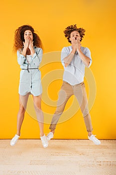 Full length portrait of amusing pleased couple man and woman 20s covering mouth with hands together, isolated over yellow