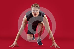 Full length portrait of athletic young runner standing on start over red studio background