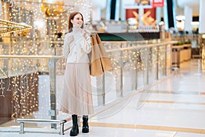 Full length portrait of attractive fashionable female model holding shopping bags on shoulder, looking away and smiling