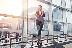 Full-length portrait of attractive model with fair hair wearing elegant formal suit standing with arms folded in airport