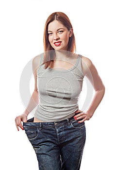 Full-length portrait of attractive slim european young smiling woman in big jeans showing successful weight loss with her happy fa