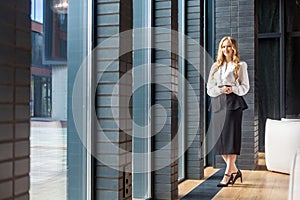 Full length portrait of attractive successful businesswoman with long blond hair in office style clothes