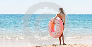 Full length portrait of attractive woman holding doughnut inflatable ring on the beach at the sea background. Have happy summer