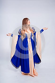 A full-length portrait of an attractive woman with long hair in a medieval, fantasy, blue and beige dress with long, large sleeves