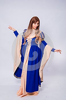 A full-length portrait of an attractive woman with long hair in a medieval, fantasy, blue and beige dress with long, large sleeves