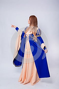 A full-length portrait of an attractive woman with long hair in a medieval, fantasy, blue and beige dress with long, large sleeves