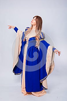 A full-length portrait of an attractive woman with long hair in a medieval, fantasy, blue and beige dress with long, large sleeves