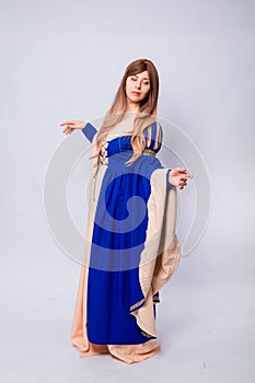 A full-length portrait of an attractive woman with long hair in a medieval, fantasy, blue and beige dress with long, large sleeves