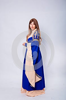 A full-length portrait of an attractive woman with long hair in a medieval, fantasy, blue and beige dress with long, large sleeves