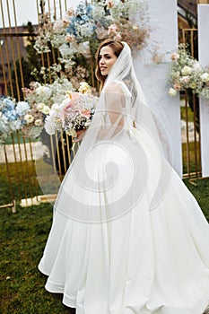 Full length portrait of attractive young bride in a white wedding dress and veil holding a big bouquet of white and pink
