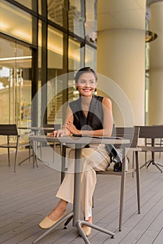Full length portrait of beautiful Asian woman sitting outdoors at coffee shop restaurant