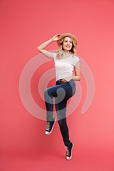 Full length portrait of beautiful blond woman 20s wearing casual jeans and straw hat smiling and walking