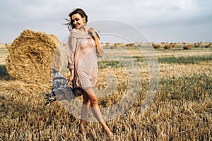 Full length portrait of a beautiful brunette in a dress and with a warm plaid. Woman enjoying a walk in a wheat field with hay