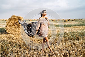Full length portrait of a beautiful brunette in a dress and with a warm plaid. Woman enjoying a walk in a wheat field with hay