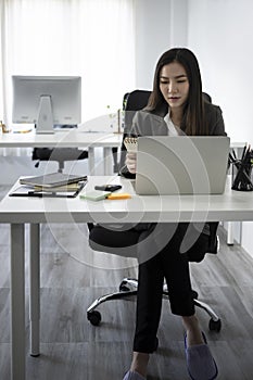 Full length portrait beautiful businesswoman sitting at office desk and using laptop computer.