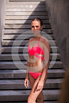 Full-length portrait of beautiful girl in the pink swimsuit with shapely body is posing near the swimming pool on