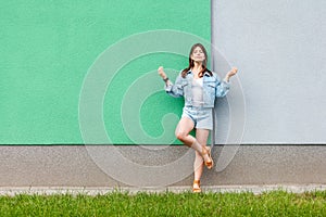 Full length portrait of beautiful woman in casual jeans denim style in summertime standing near green and light blue wall and