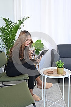 Full length portrait beautiful woman drinking coffee and reading book at home.