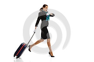 Full-length portrait of beautiful young woman, flight attendant running with suitcase isolated on white studio