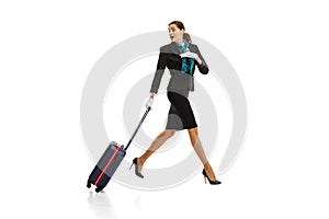 Full-length portrait of beautiful young woman, flight attendant running with suitcase isolated on white studio