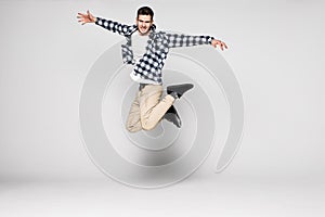 Full length portrait of a casual young man jumping with hands outstretched isolated over white background