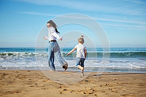 Full length portrait of Caucasian authentic family of a young mother and cute daughter running barefoot on the beach