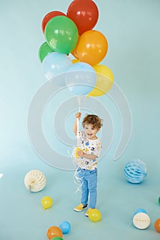 Full length portrait of cheerful boy holding balons posing against blue background