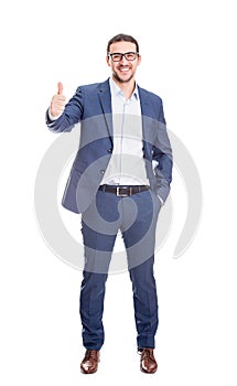 Full length portrait, cheerful businessman smiling broadly showing thumb up gesture isolated on white background. Contented