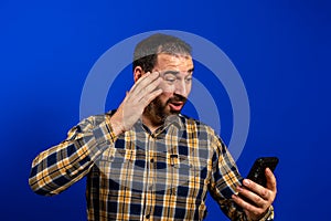 Full length portrait of a cheerful handsome young man standing isolated over blue background, holding mobile phone.