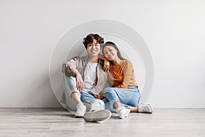 Full length portrait of cheerful young Asian couple in casual outfits sitting on floor and looking at camera