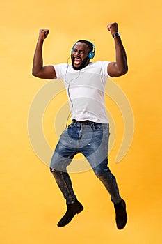 Full length portrait of a cherry young african american man listening to music with headphones and dancing isolated over