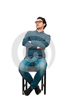Full length portrait of confident businessman seated relaxed on a chair, wearing eyeglasses and keeps arms crossed, isolated on