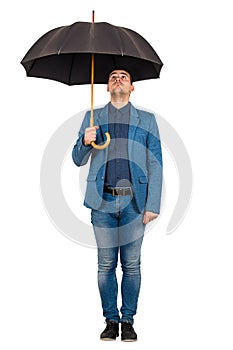 Full length portrait of confused businessman standing under open umbrella looking up perplexed isolated over white background