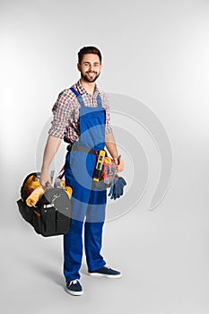 Full length portrait of construction worker with tools on light background