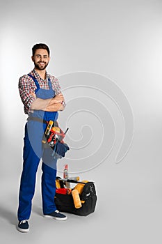 Full length portrait of construction worker with tools on light background
